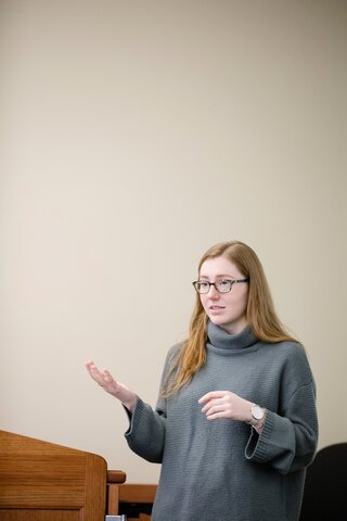 Female student with red hair and grey sweater presents at a KIN undergraduate course