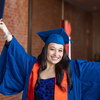A female student in graduationg regalia spreads her arms holding a diploma