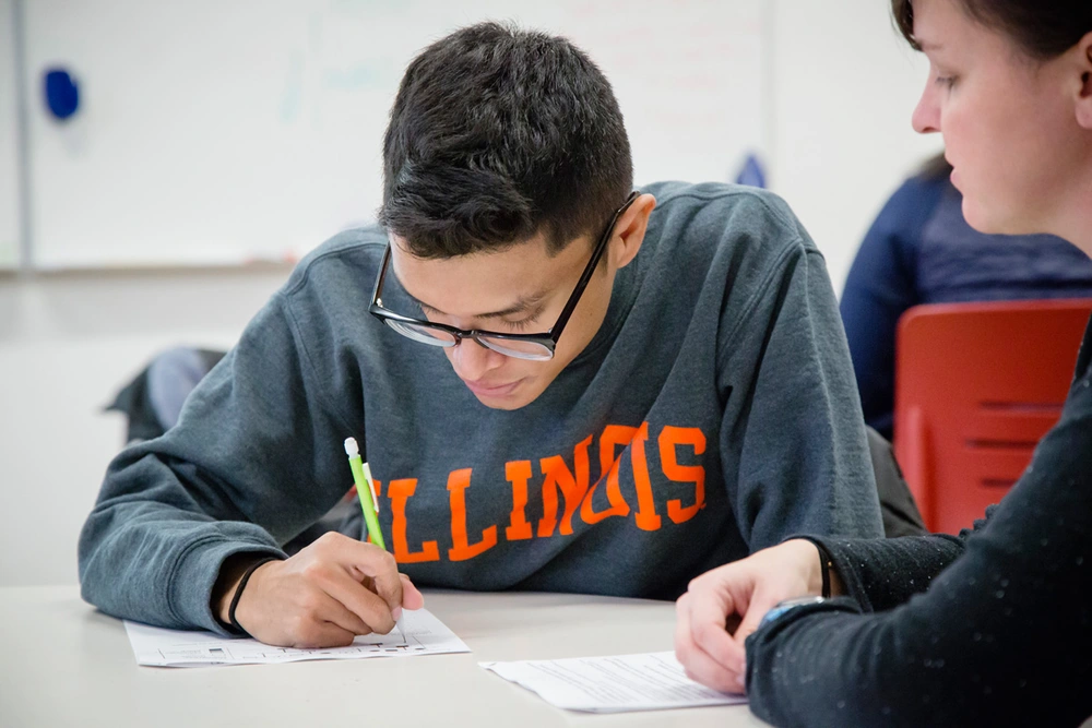 A female teaching assistant helps a male undergraduate student with an assignment during class.